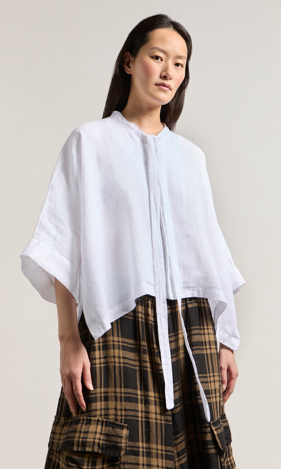 Plümo- Person wearing the Antoine Blouse - White with ribbon necktie and wide sleeves, paired with a brown plaid skirt.