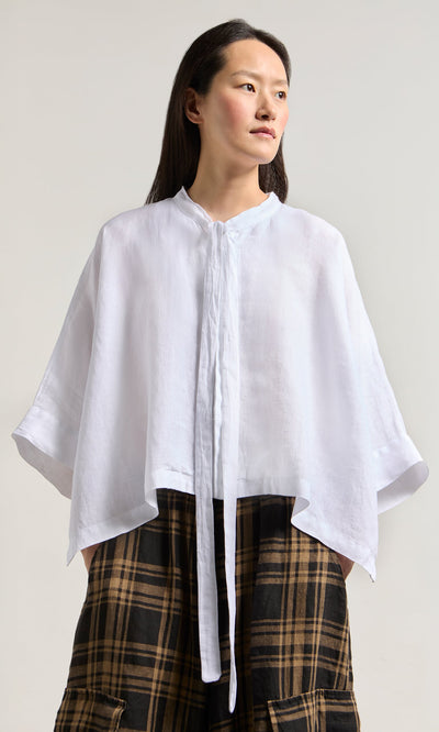 Plümo- Woman in the Antoine Blouse - White, made in Greece, styled with a ribbon necktie and plaid skirt on a light background.