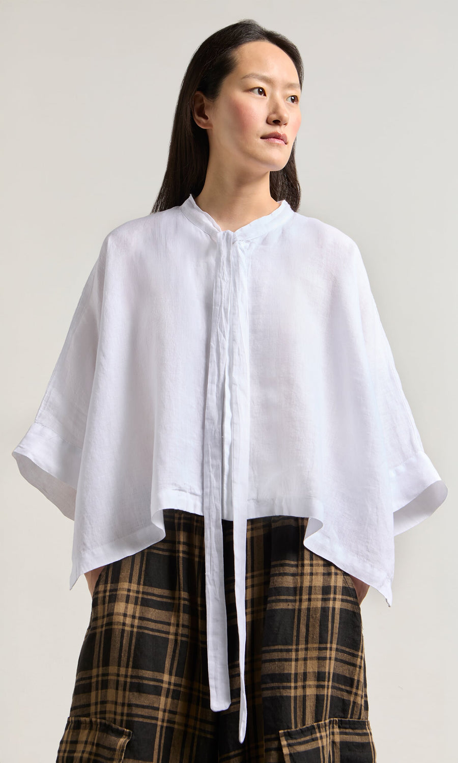 Plümo- Woman in the Antoine Blouse - White, made in Greece, styled with a ribbon necktie and plaid skirt on a light background.