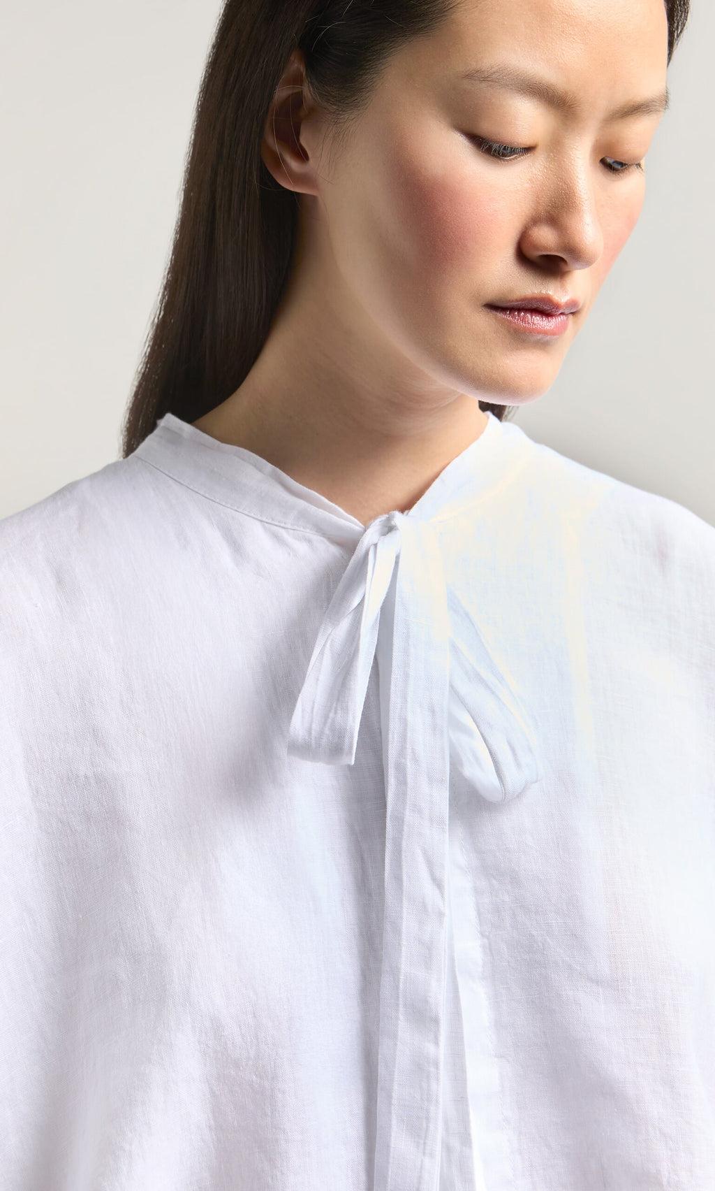 Plümo- Woman models the Antoine Blouse in white, featuring a ribbon necktie, against a plain background.