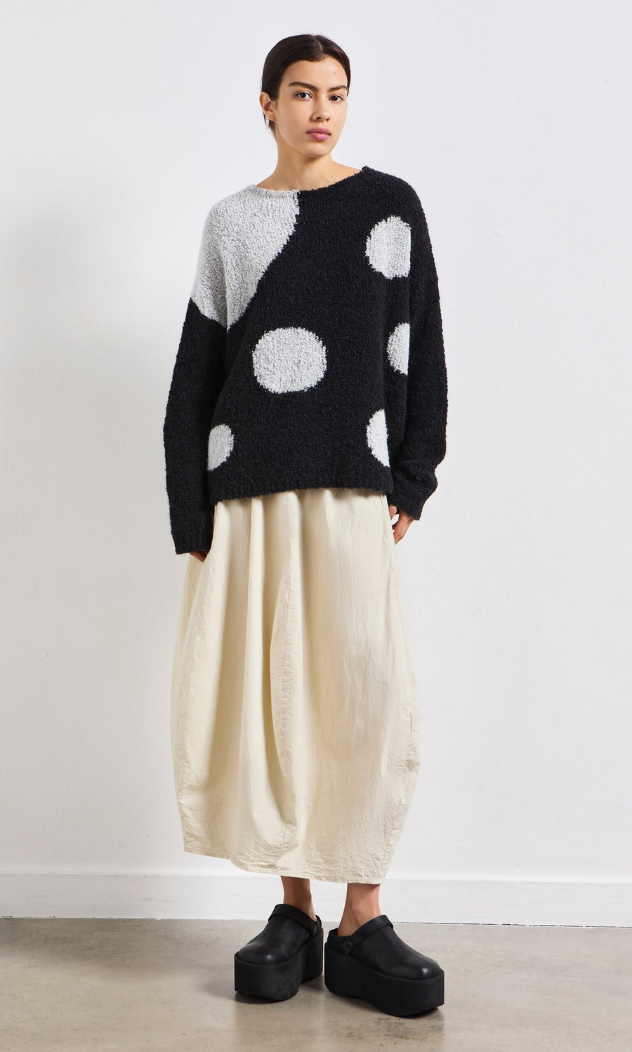 Plümo- Woman wearing the Antra Spot Jumper, a handcrafted Italian polka dot sweater, standing indoors.