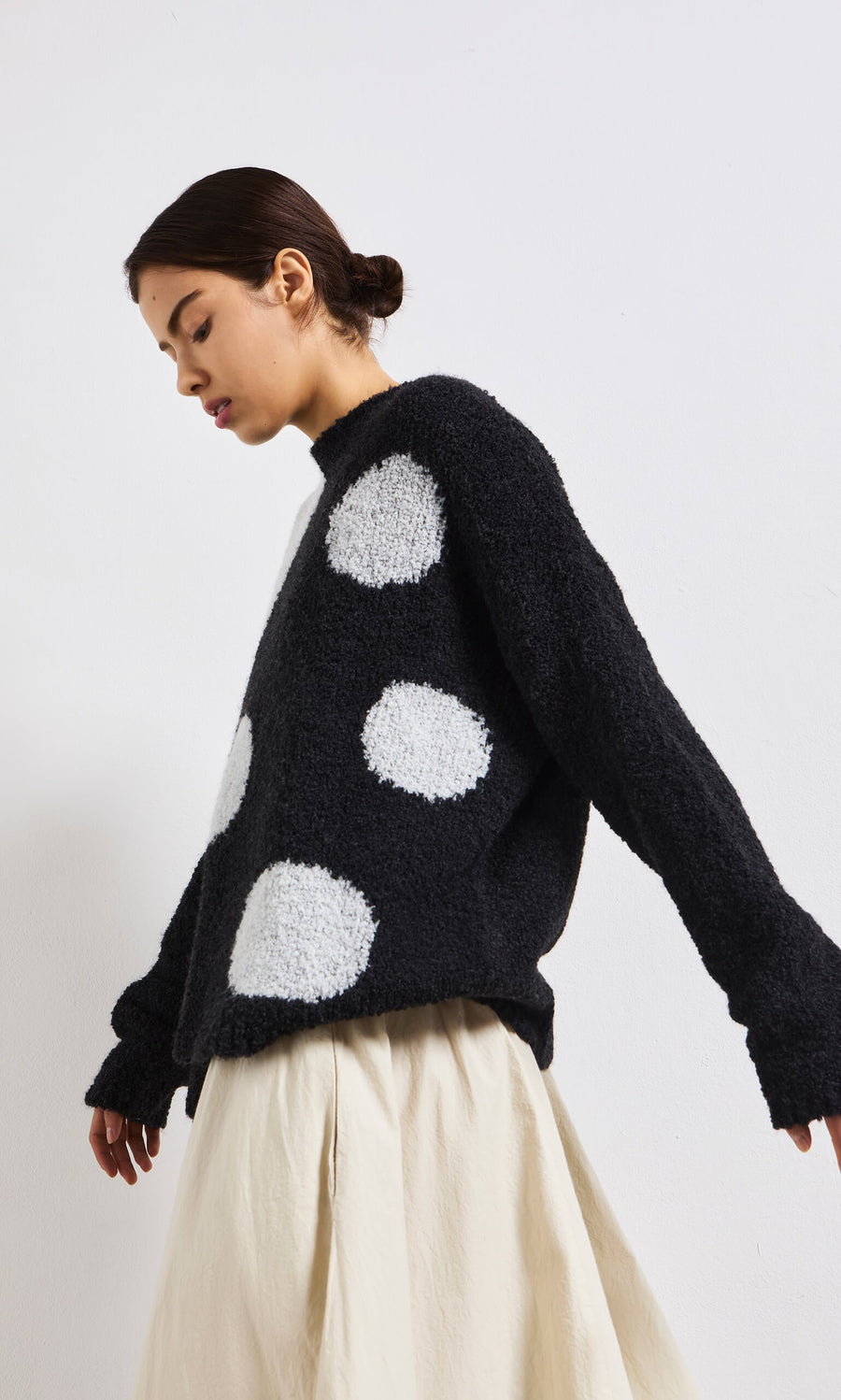 Plümo- Woman wearing the Antra Spot Jumper, a lightweight black knit with large white polka dots, and a cream skirt.
