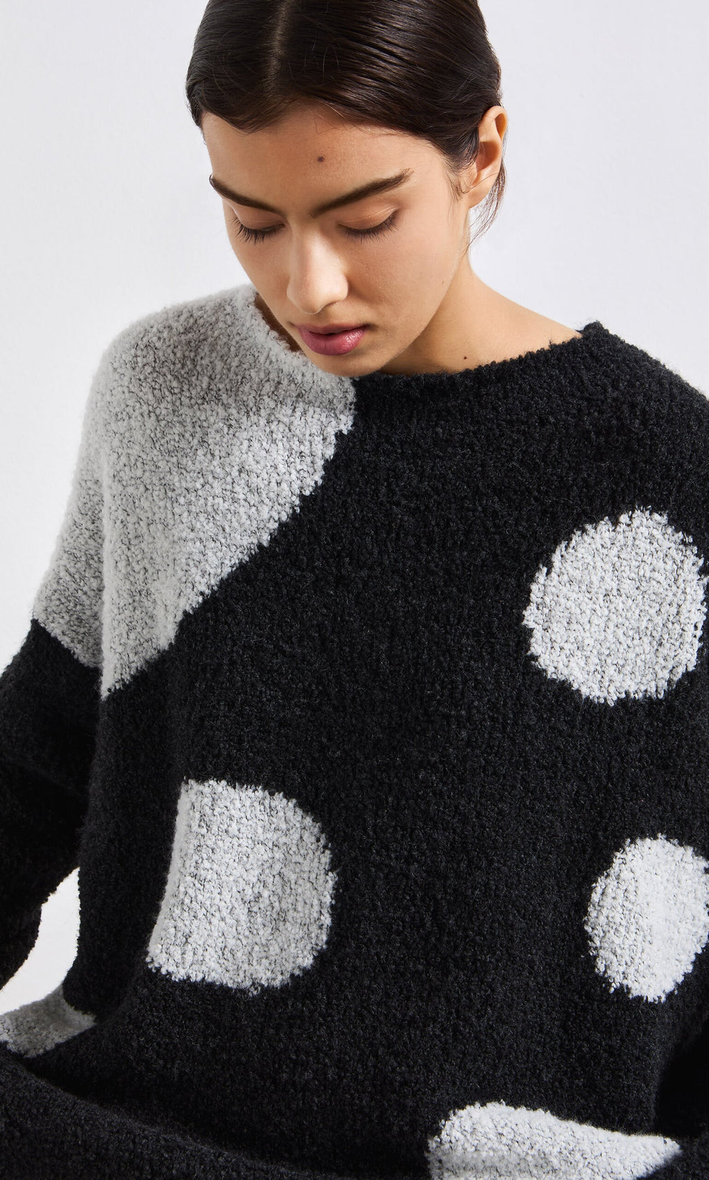 Plümo- A woman in the Antra Spot Jumper, a handcrafted Italian black and white fleece sweater with large polka dots, looks down.