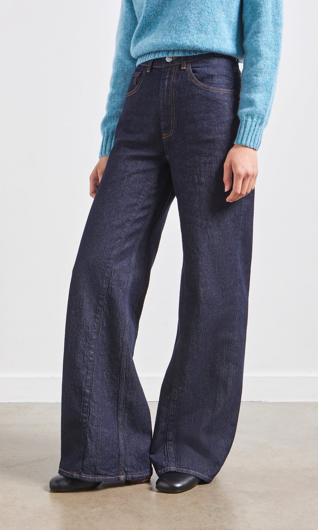 Plümo- Person wearing Belted Wide Jeans, a light blue sweater, and black shoes, standing indoors on a light floor.
