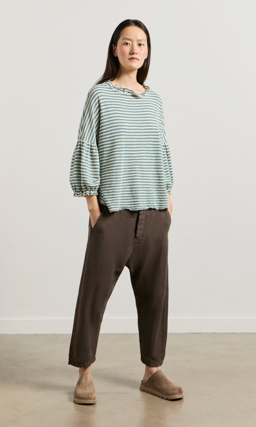 Plümo- Woman in striped top and Caper Pants - Brown: relaxed fit, tapered leg, hands in pockets.