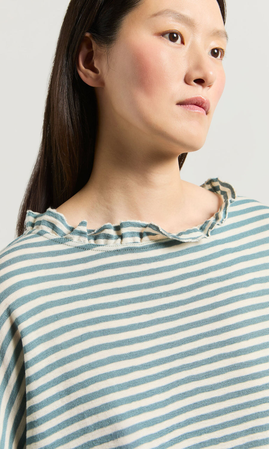 Plümo- A person wears the Blue Stripe Ruffle Blouse, looking slightly to the side.