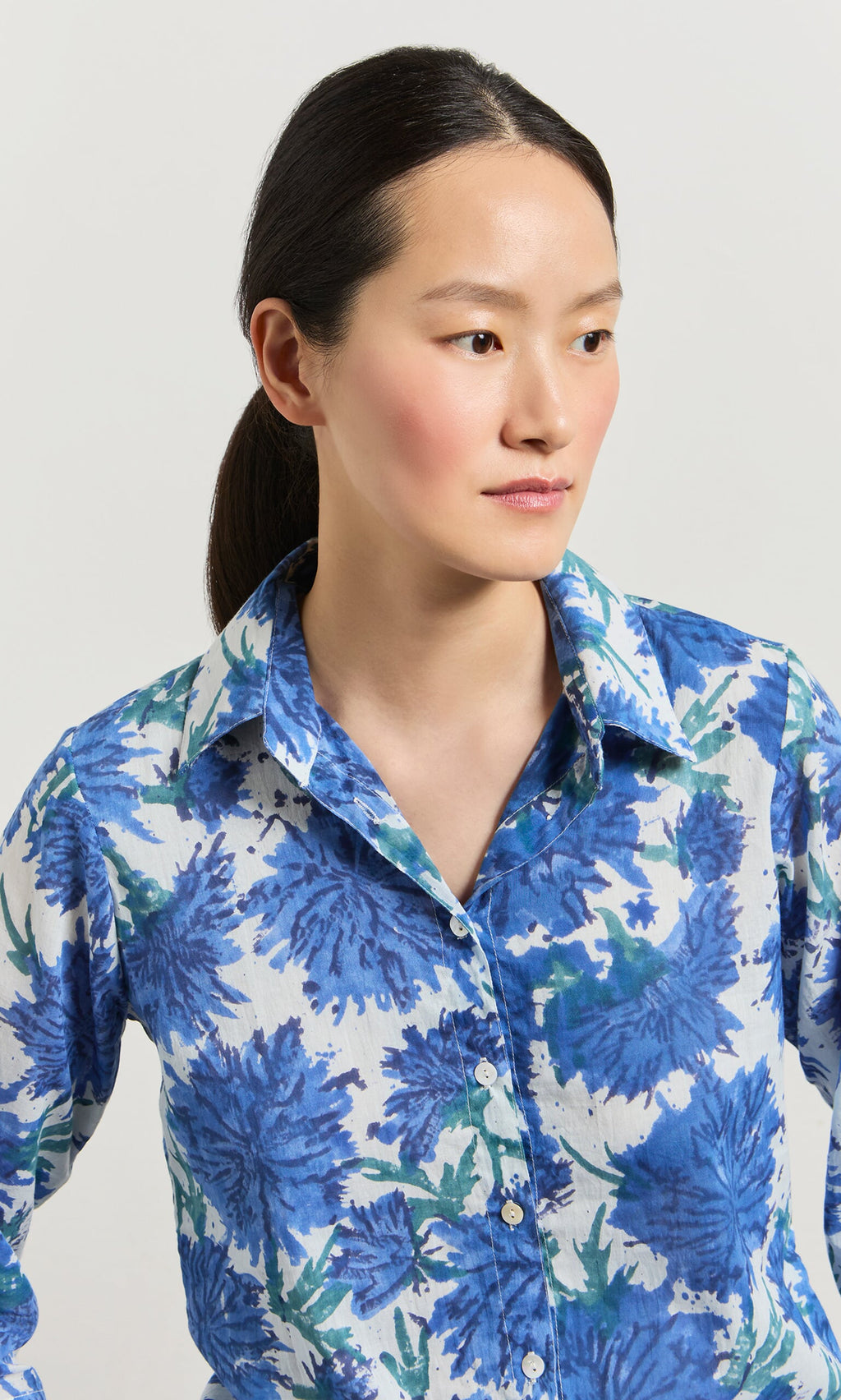 Plümo- Woman with dark hair in a ponytail wears the Blue Thistle Shirt, looking to the side.