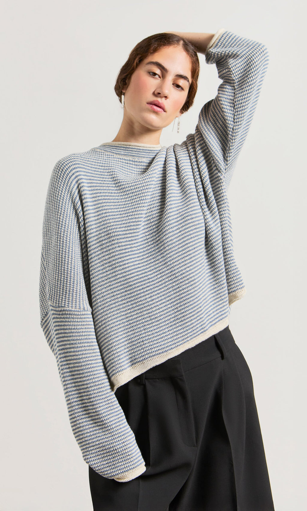 Plümo- Woman wearing the Boathouse Jumper—relaxed fit, striped cotton sweater—poses with one arm raised against a plain background.