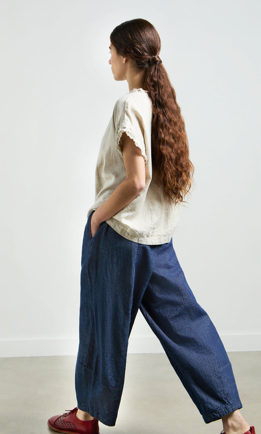 Plümo- Woman with long brown hair in a relaxed silhouette, wearing the Birch Ruffle Top and blue wide-leg pants indoors.