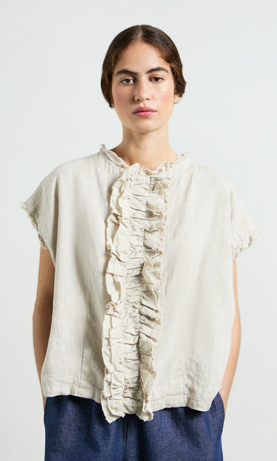 Plümo- Woman wearing the Birch Ruffle Top and blue pants, standing against a plain light background.