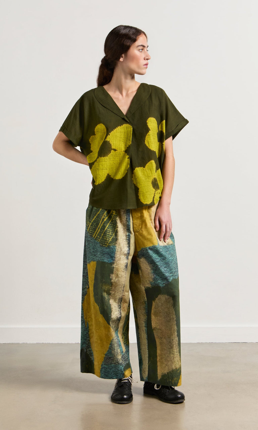 Plümo- Woman wears Brushstroke Pants and a green and yellow floral top, looking to the side.