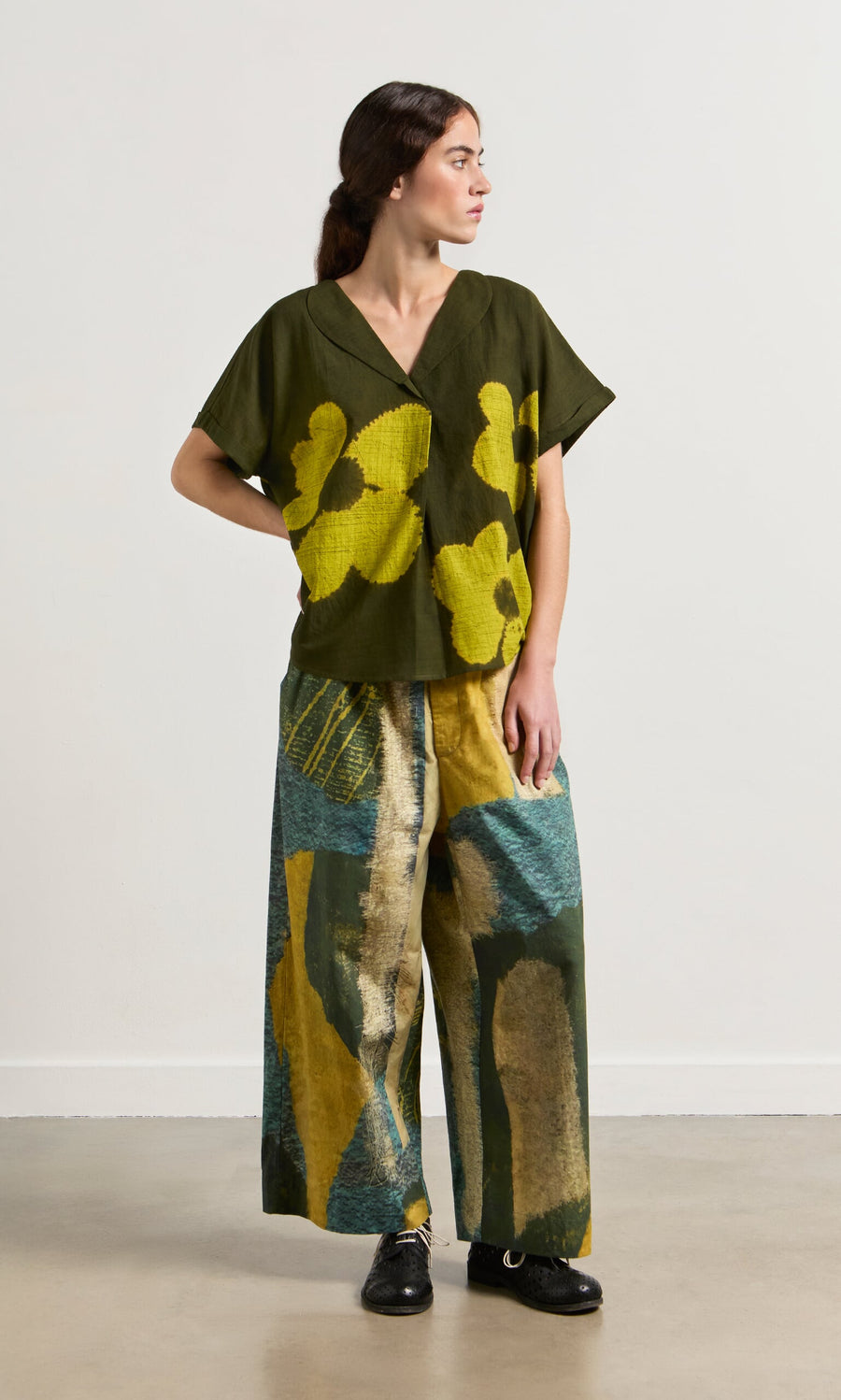 Plümo- Woman wears Brushstroke Pants and a green and yellow floral top, looking to the side.
