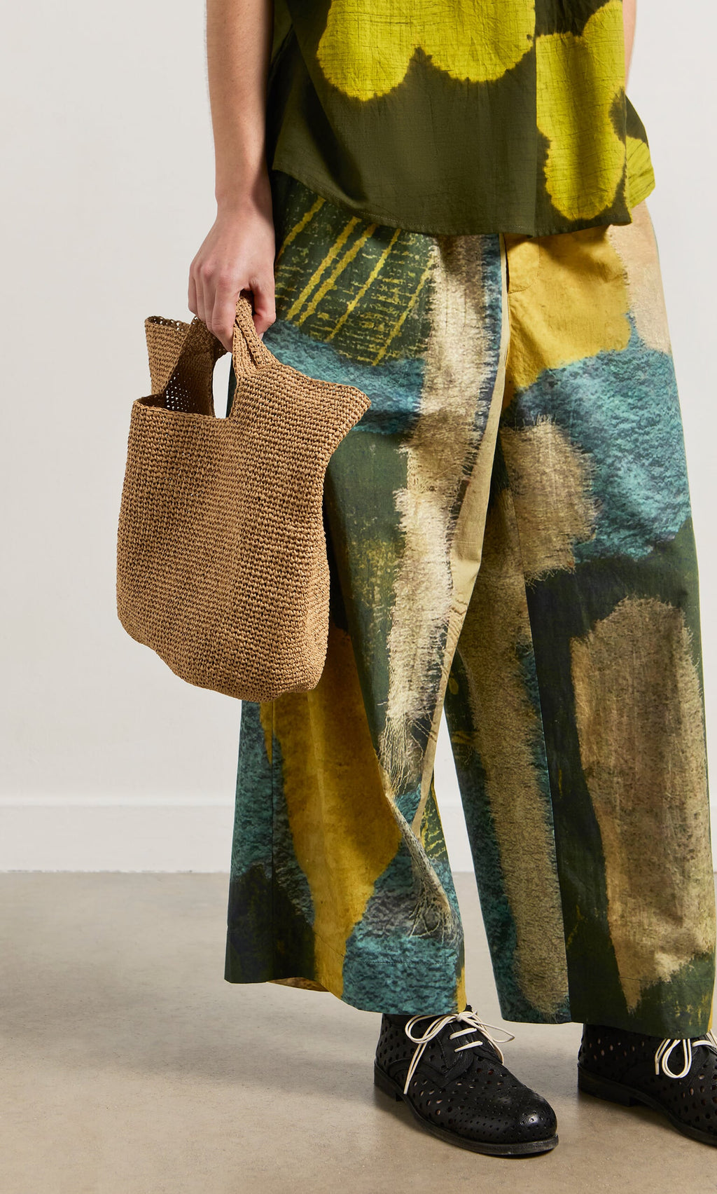Plümo- Person wearing Brushstroke Pants with an elasticated drawstring waist, black shoes, tan woven bag, and green top.