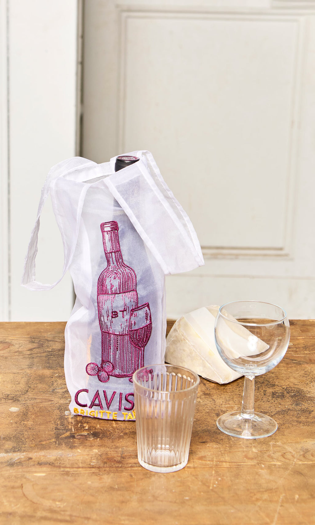 Plümo- A Caviste Wine Bottle Gift Bag, two glasses, and a wedge of cheese sit on a wooden table.