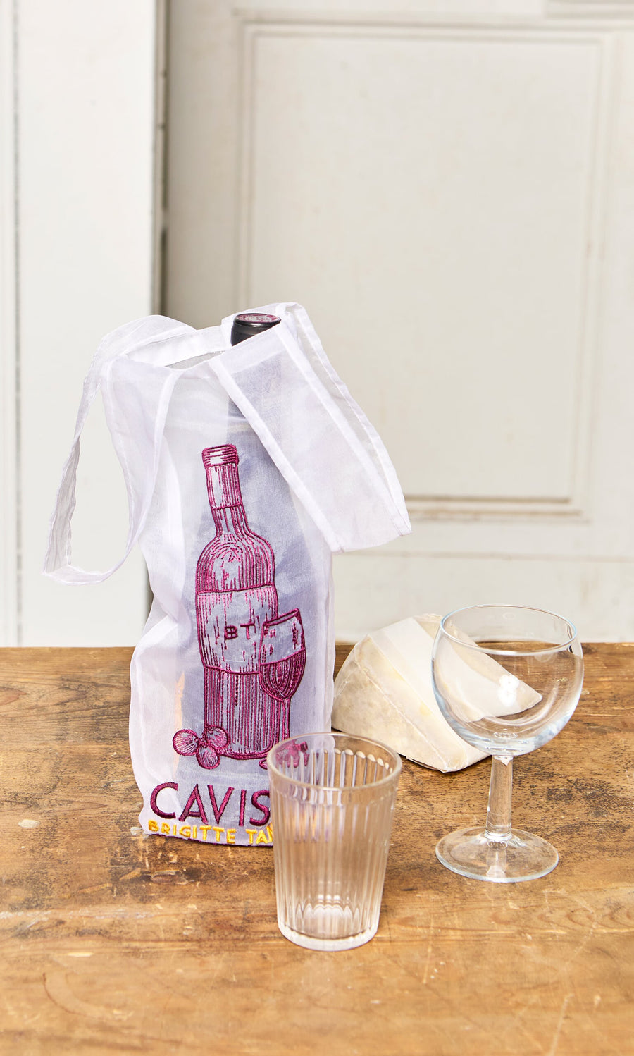Plümo- A Caviste Wine Bottle Gift Bag, two glasses, and a wedge of cheese sit on a wooden table.