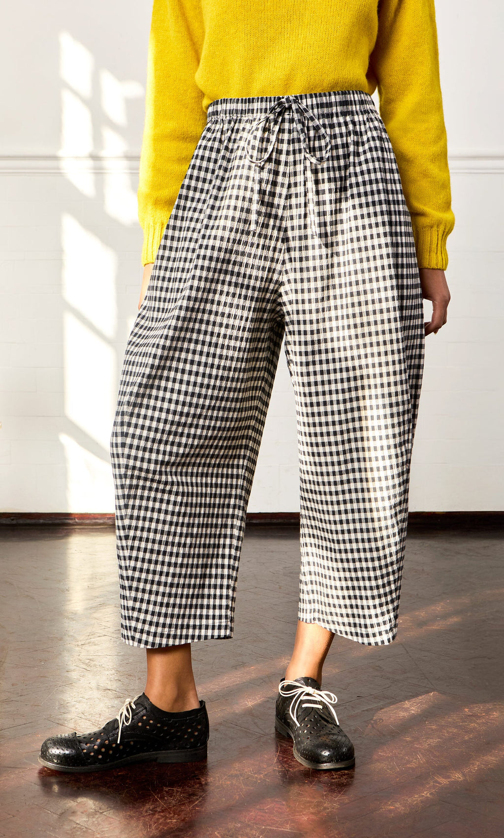 Plümo- Person wearing Butoni Pants - Black and White, a yellow sweater, and black shoes, standing indoors.