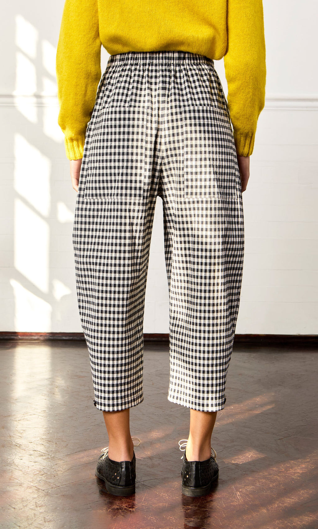 Plümo- Person wearing Butoni Pants - Black and White with a yellow sweater and black shoes in the sunlight.