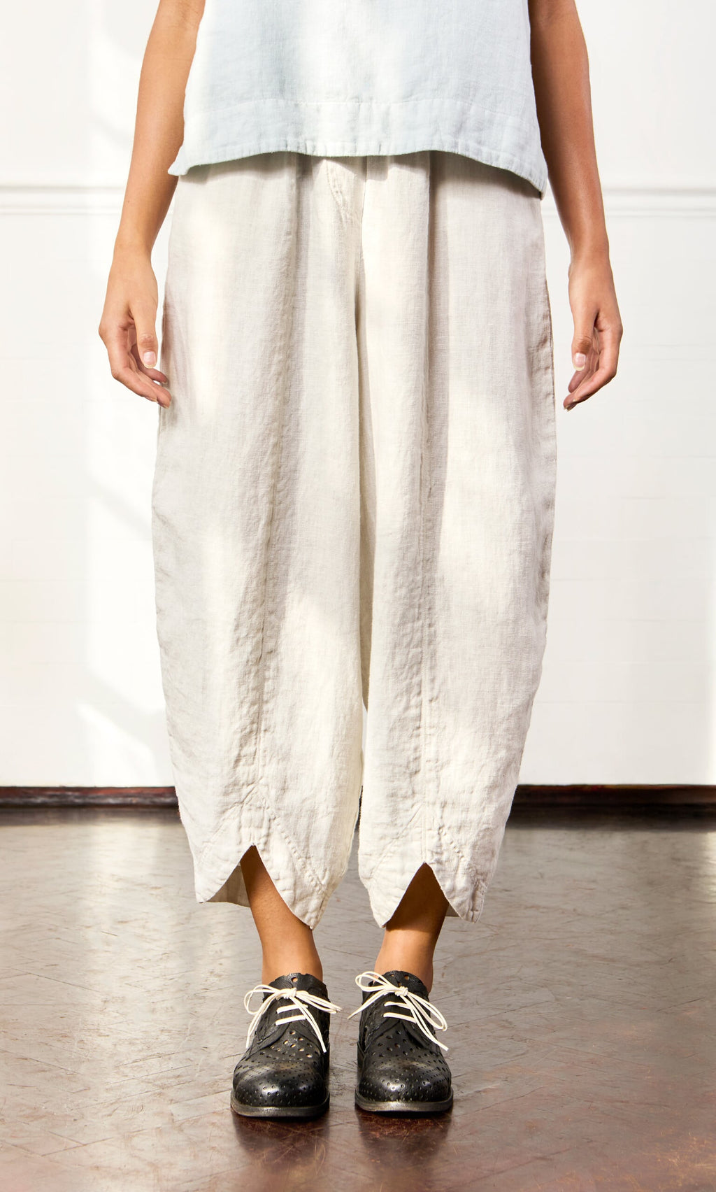 Plümo- A person wearing Cazalla Pants with an elastic waist and black shoes stands on a brown floor.
