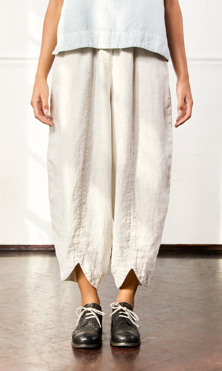 Plümo- A person wearing Cazalla Pants with an elastic waist and black shoes stands on a brown floor.