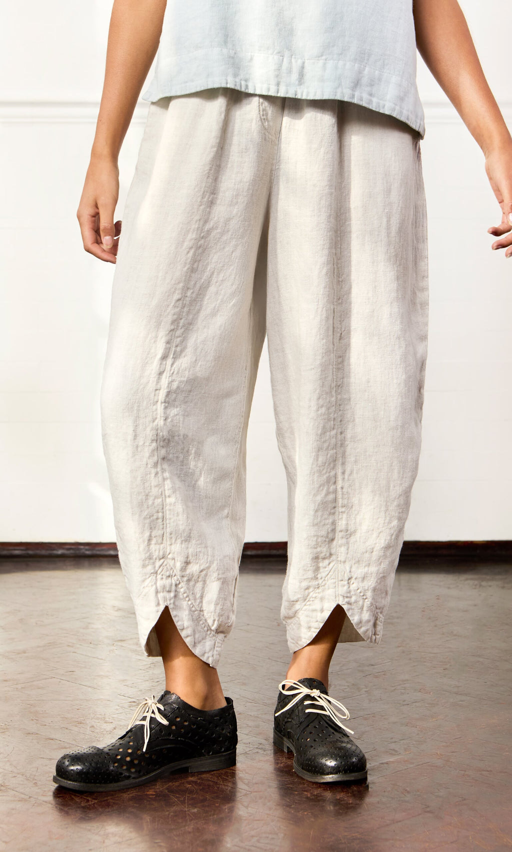 Plümo- Someone wearing Cazalla Pants—light linen, loose fit, elastic waist—and black lace-up shoes, standing on wood floor.