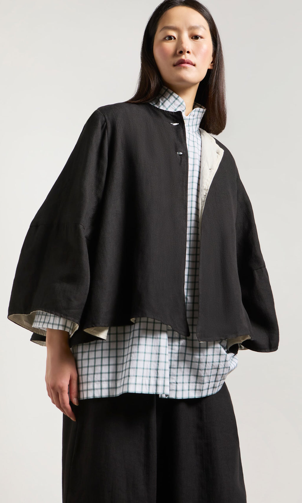 Plümo- Woman in a loose black Holden Jacket with shoulder pads, over a checkered shirt and wide black pants.