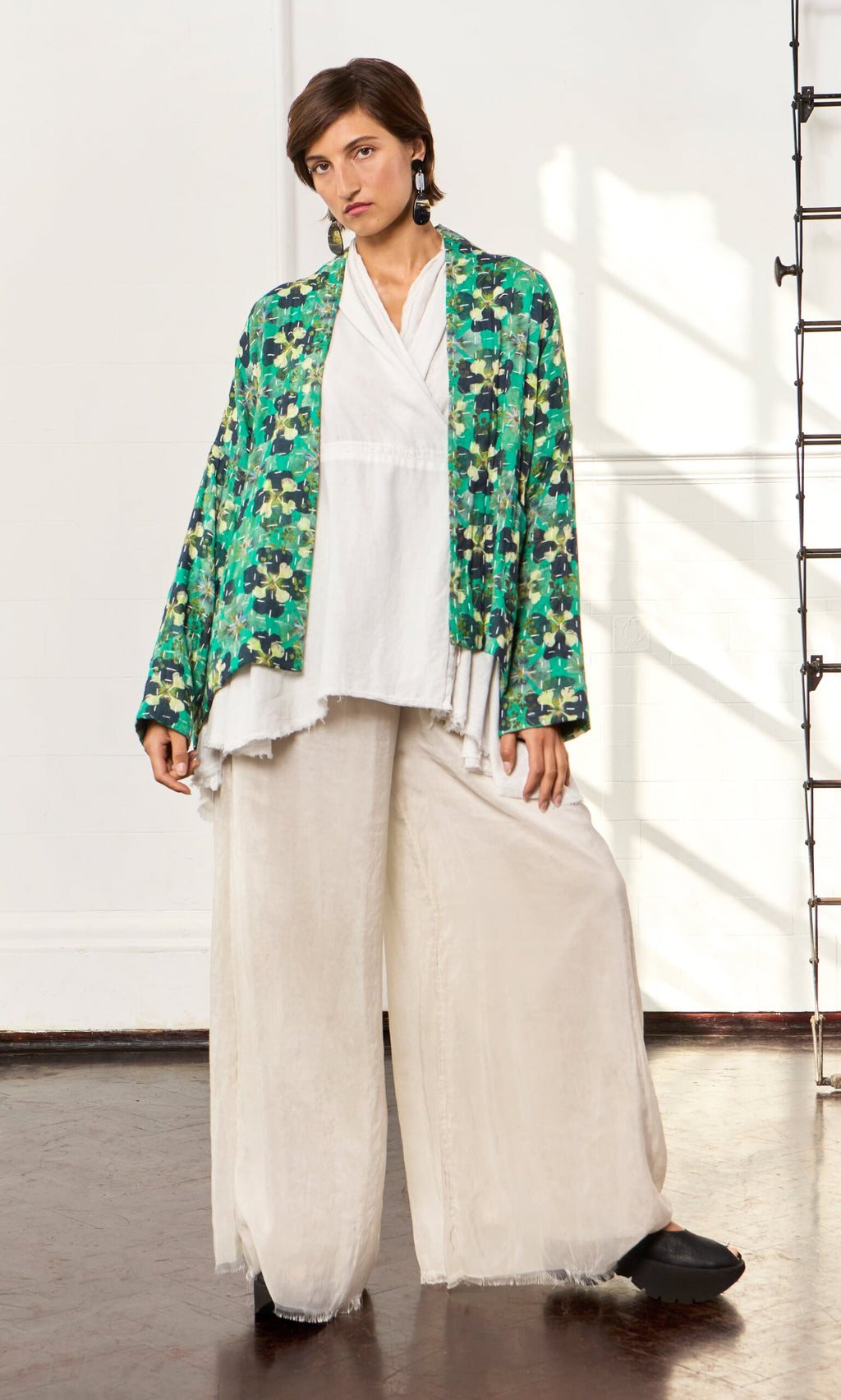 Plümo- A person in a white top and Clover Jacket stands indoors by a white wall and ladder.