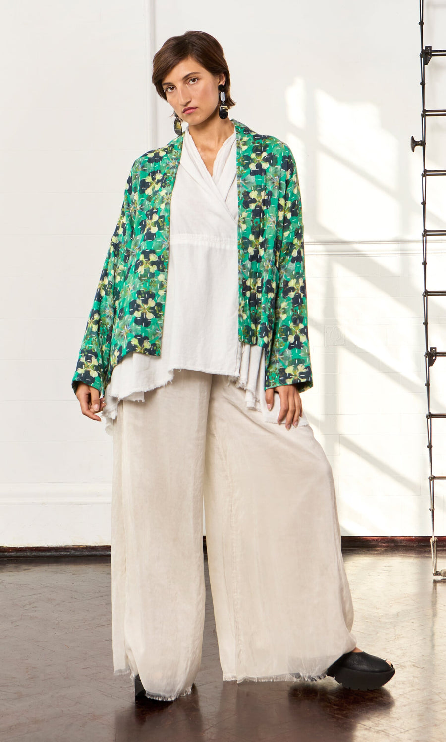 Plümo- A person in a white top and Clover Jacket stands indoors by a white wall and ladder.