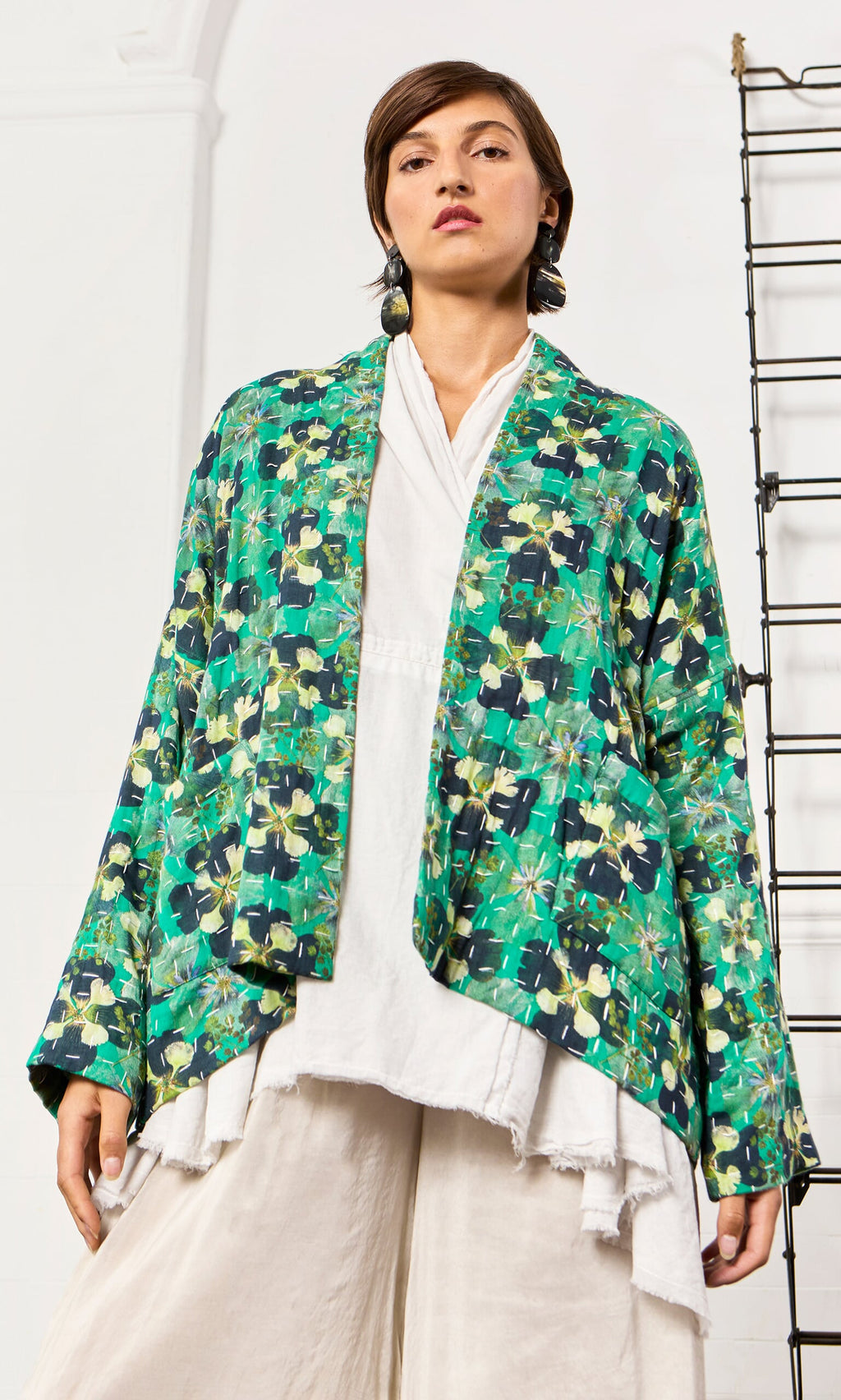 Plümo- Woman wearing the Clover Jacket in a relaxed pansy print over a white top and wide cream pants against a white background.