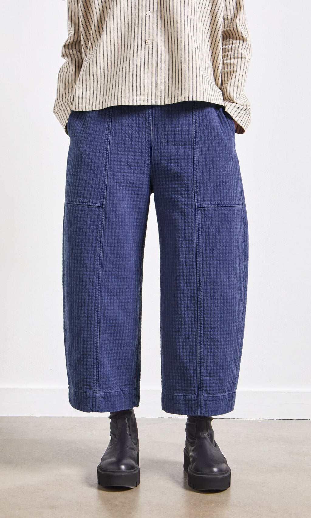 Plümo- Person wearing a striped beige shirt, Calow Pants in textured blue, and black boots, standing against a white background.