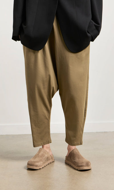 Plümo- Person wearing tan Mirana Pants, brown suede clogs, and a black jacket on a light-colored floor.