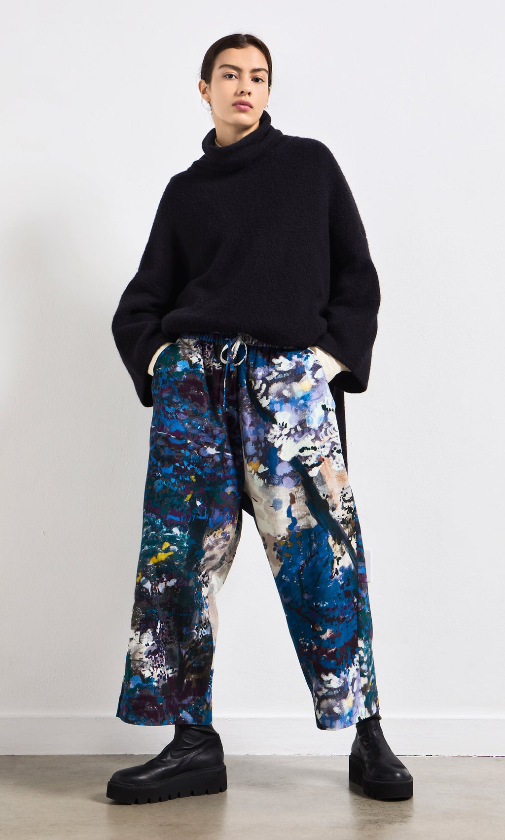 Plümo- Woman in a black turtleneck, Covey Pants with elastic waist, and black platform boots.