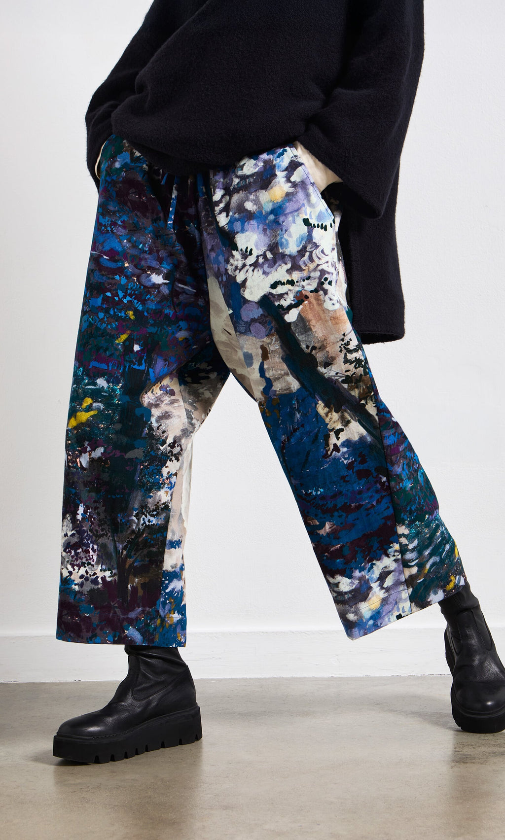 Plümo- Person wearing Covey Pants, a black sweater, and black boots on a concrete floor.