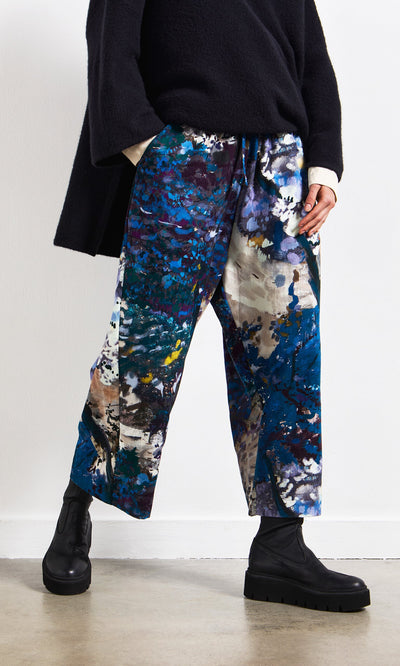 Plümo- Person wearing Covey Pants, black boots, and a black sweater, standing indoors by a white wall.