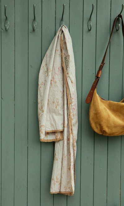 Plümo  The Dawn Scarf, a crinkly cotton piece with vintage florals, hangs by a tan suede bag on animal hooks; fairtrade-made.