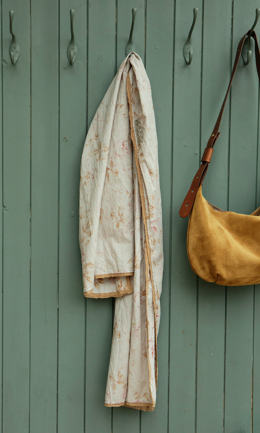 Plümo  The Dawn Scarf, a crinkly cotton piece with vintage florals, hangs by a tan suede bag on animal hooks; fairtrade-made.