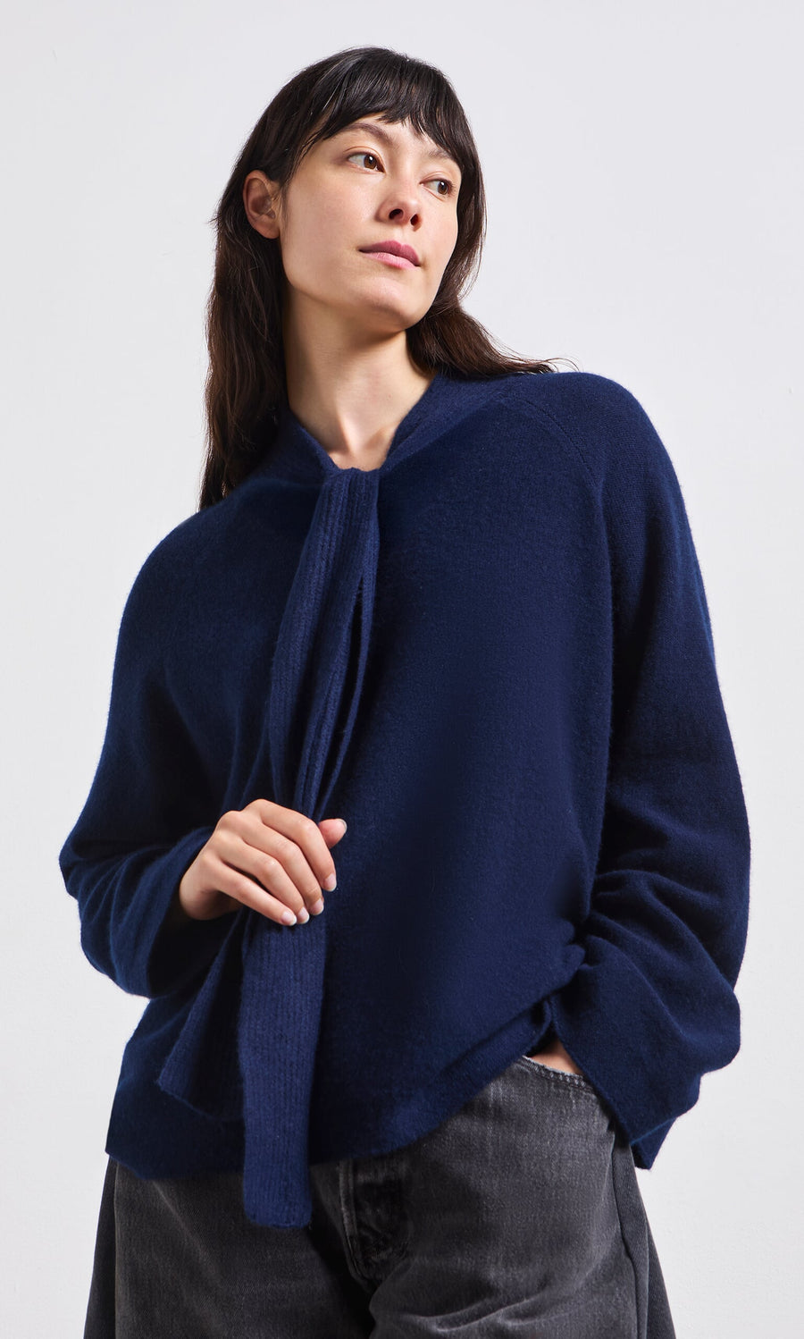 Plümo- Woman wearing the Dobbs Jumper, a navy blue sweater with rib knit ties, standing with one hand in her pocket.