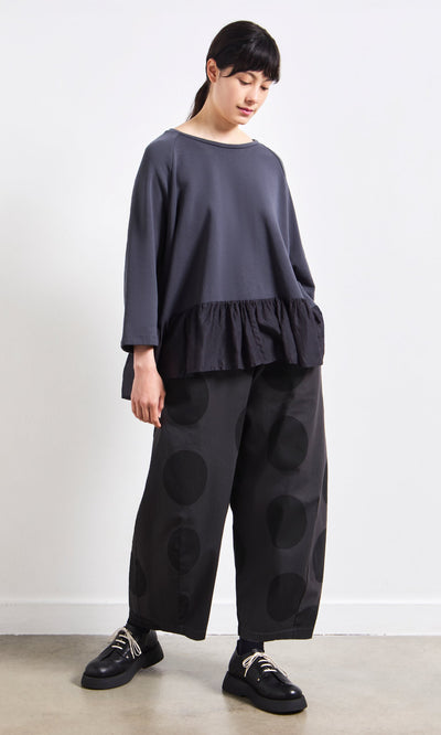 Plümo- Woman in a loose gray ruffled top and Easy Point Pants—modern polka-dot cotton canvas, handcrafted in Italy.