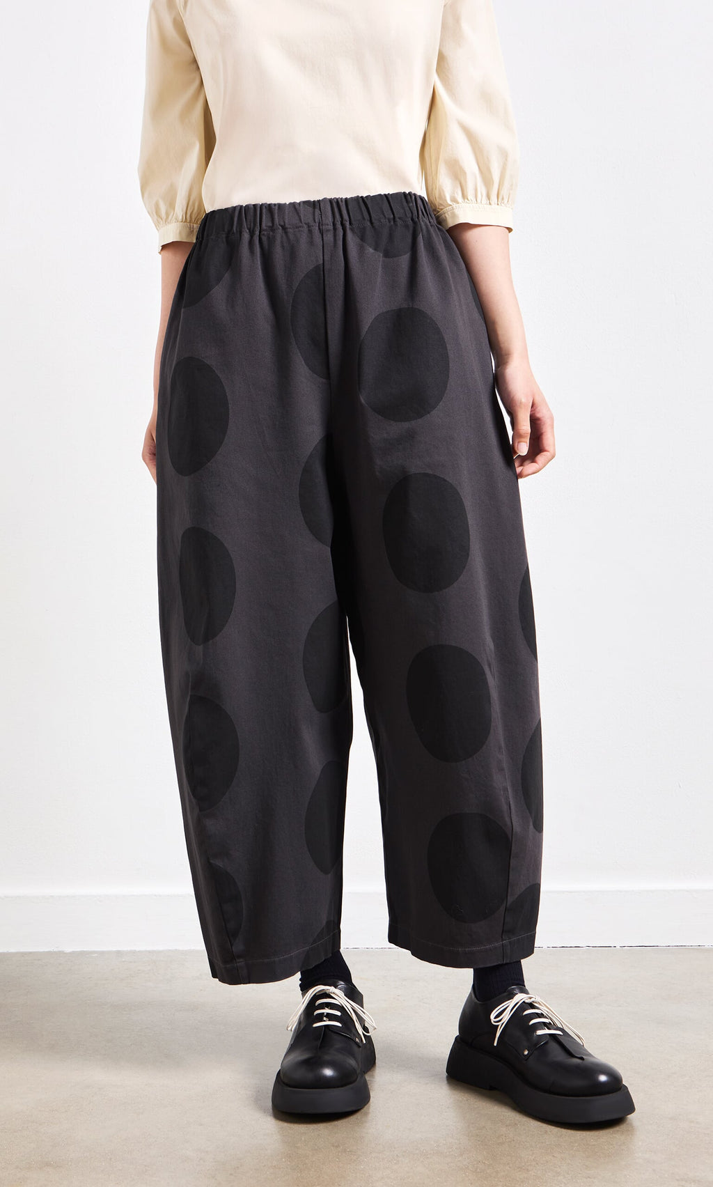 Plümo- Person wearing Easy Point Pants with large black polka dots, black shoes, and a cream top.
