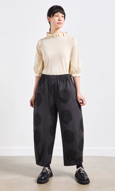Plümo- Person standing wearing a cream blouse with ruffled collar and Easy Point Pants in large polka-dot cotton-canvas.