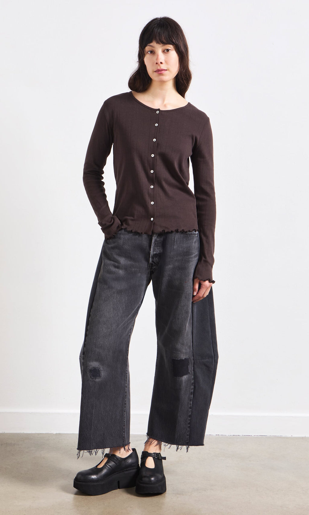 Plümo- Woman in the GOTS certified Eddie Cardigan, black wide-leg jeans, and platform shoes against a plain background.