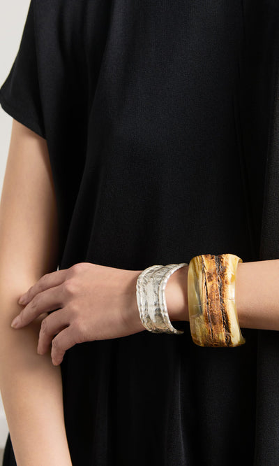 Plümo- A person in a black top wears an artisan bracelet and the Ember Cuff on their left wrist.