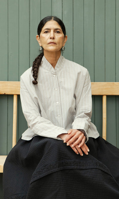 Plümo  A woman with a long braid, striped shirt, and dark skirt sits on a bench wearing Tamsin Earrings.