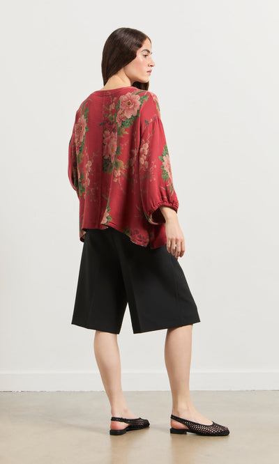 Plümo- Woman facing away, wearing the Frida Blouse, black knee-length shorts, and black flats on a light floor.