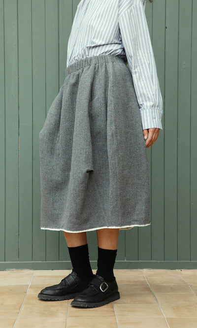 Plümo  Person wearing the Ghent Skirt, striped shirt, black socks, and loafers stands on a tiled floor.