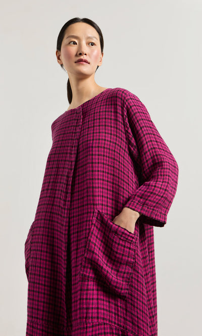 Plümo- Woman in the Gilda Check Dress—an oversized, long-sleeve linen dress with windowpane checks and large pockets.