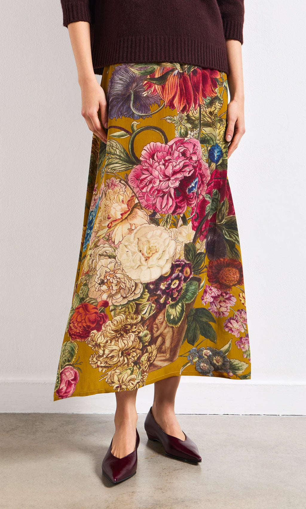 Plümo- Person wearing the Golda Skirt, a vintage-inspired floral design, with burgundy flats indoors.