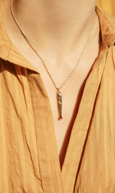 Plümo- A person wearing a mustard yellow collared shirt and the Sardine Necklace.