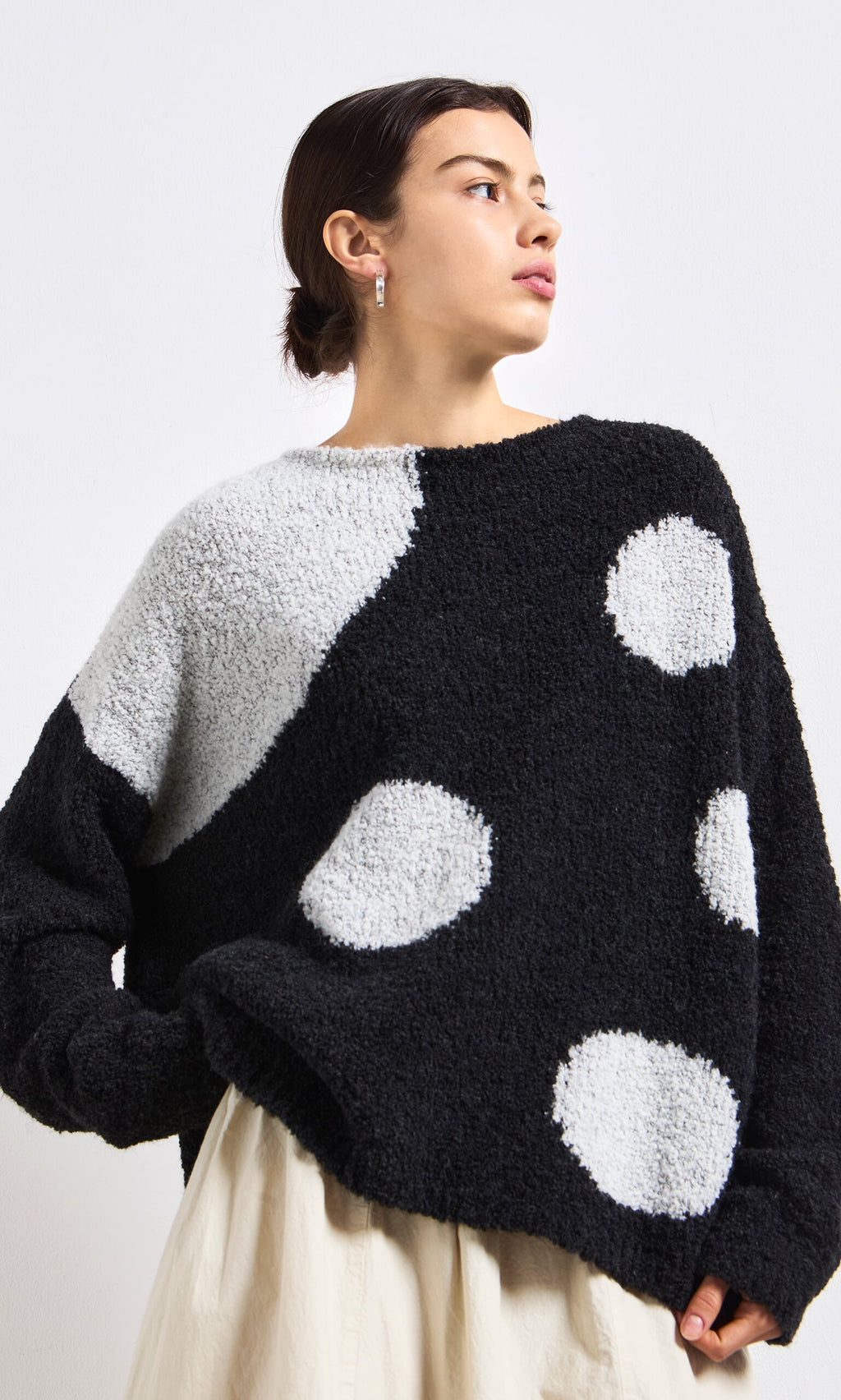 Plümo- Woman in Antra Spot Jumper, a lightweight black and white polka dot sweater, with cream skirt against a white background.