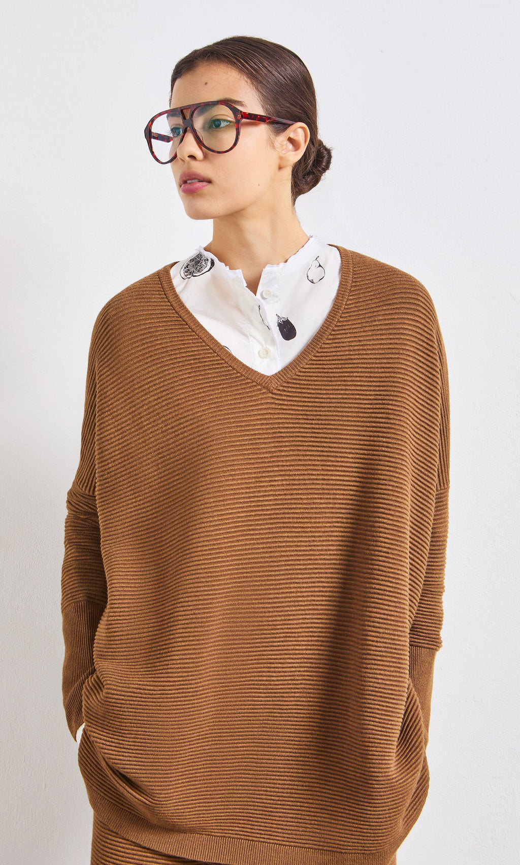 Plümo- Woman in oversized brown ribbed sweater, white embroidered shirt, and Havana Red Readers, looking sideways.