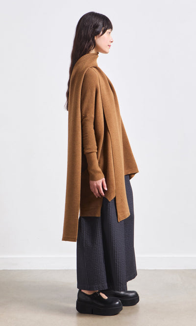 Plümo- Woman in a brown draped cardigan, Janie Scarf - Chestnut, wide-leg black pants, and platform shoes, standing sideways.